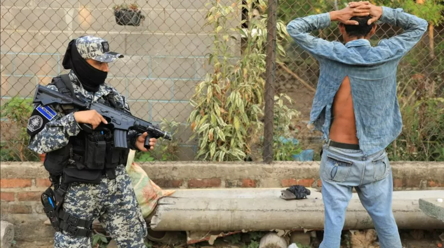 عنصر من شرطة السلفادور يوجه سلاحه إلى أحد الأشخاص الذي يضع يديه فوق رأسه