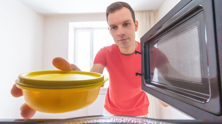 Homem colocando pote plástico no micro-ondas