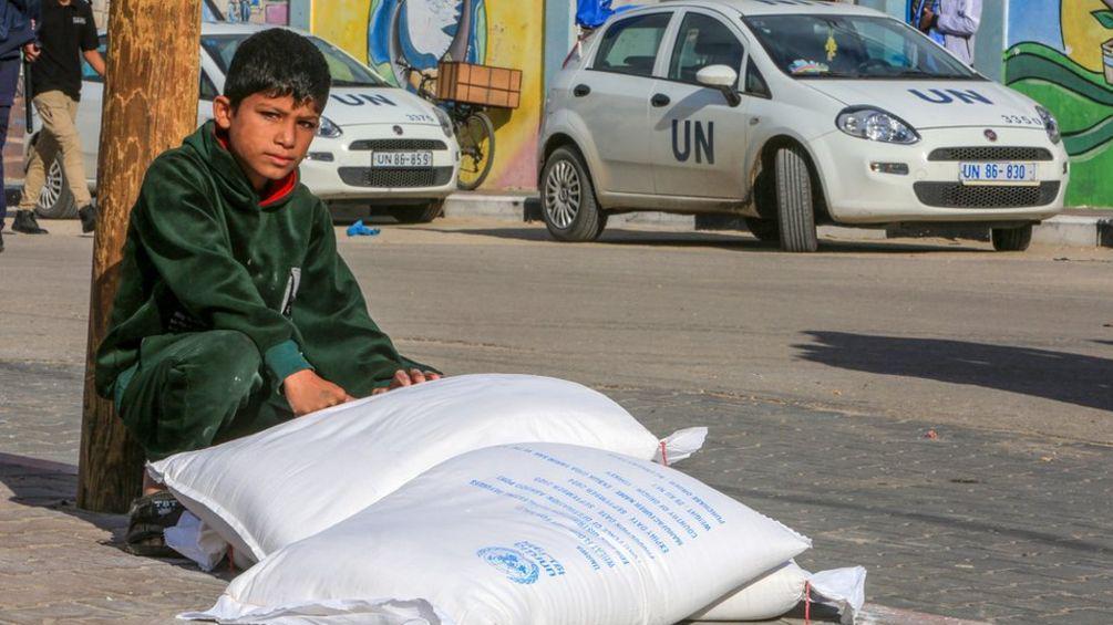 Criança ao lado de mantimentos pela agência da ONU em Gaza