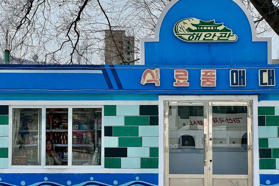 朝鮮一家食品店的外觀照片。有個女人正在往窗外看