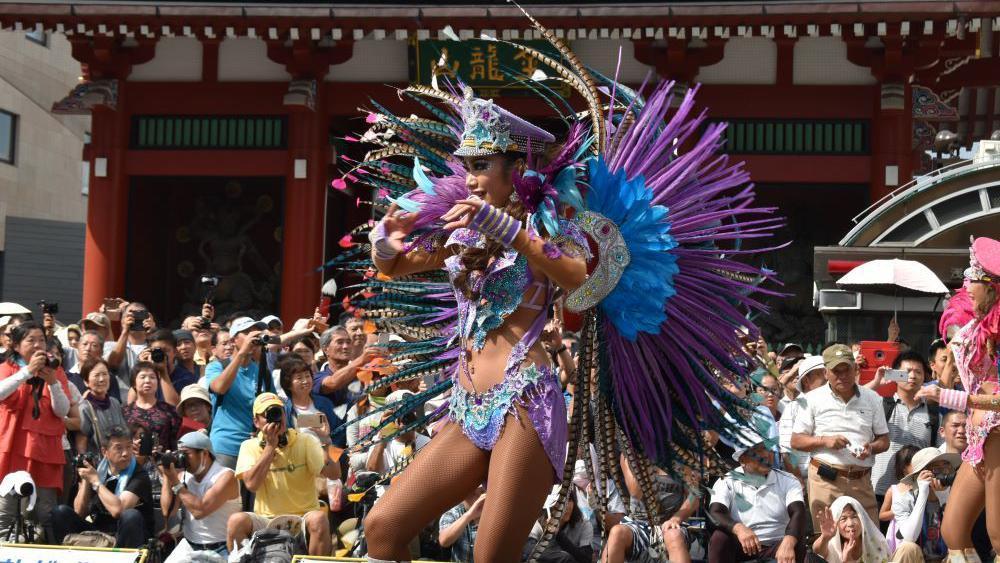 Imagem de uma mulher desfilando com uma fantasia de plumas nos tons de azul e lilás.