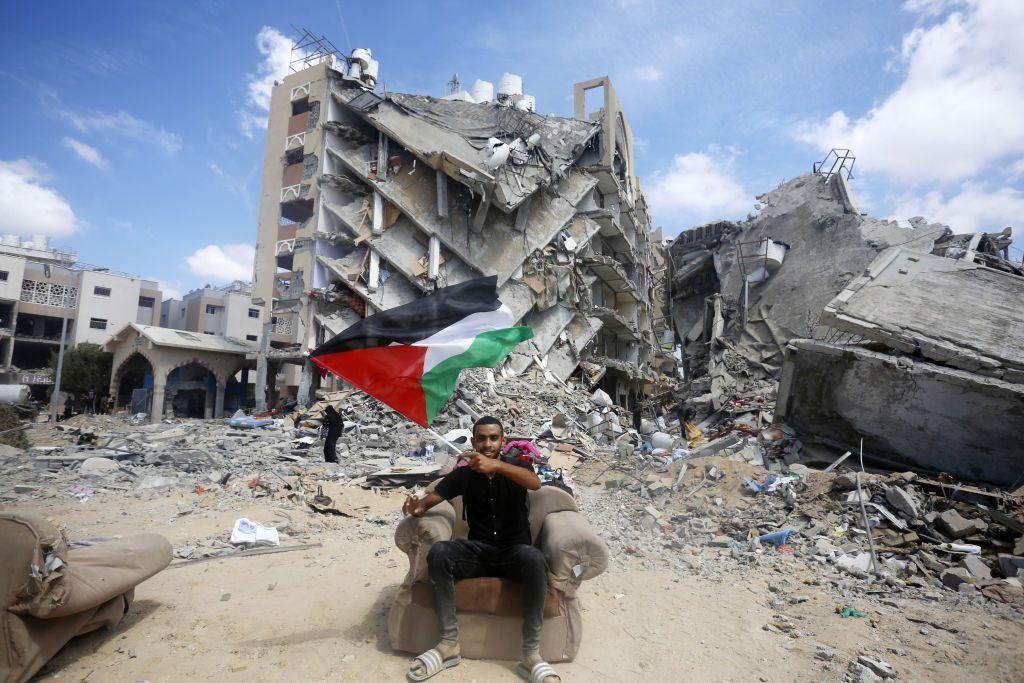 Um homem agita uma bandeira palestina em meio às ruínas de Gaza.