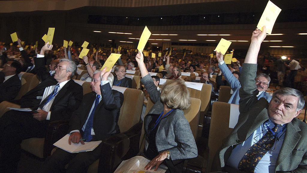 Pessoas sentadas levantando cédulas de voto