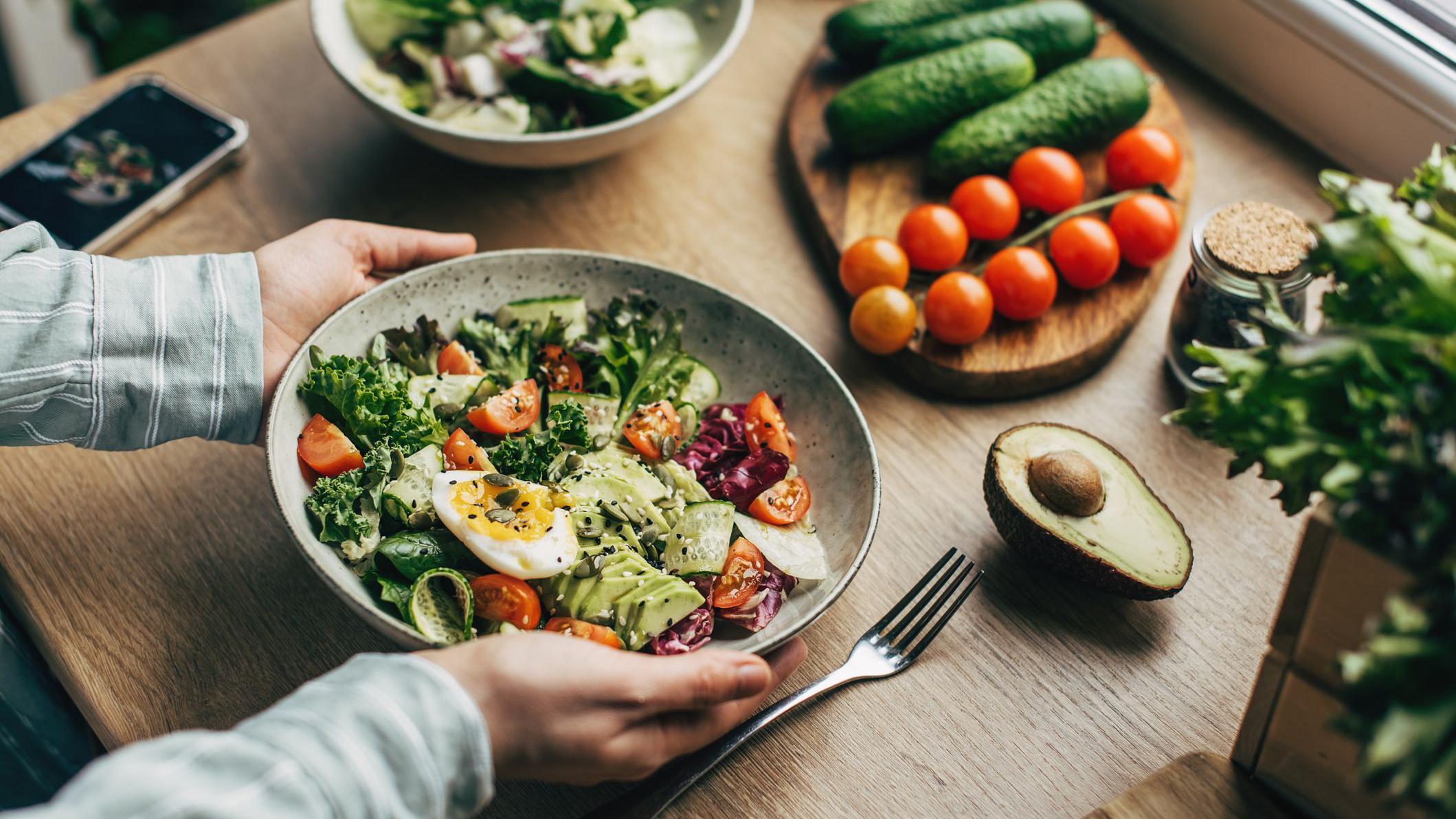 Una mesa con ensalada, palta, tomates y pepino.