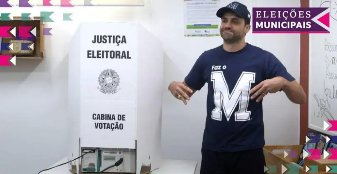 Pablo Marçal usando camisa azul com a letra M estampada em uma cabine de votação