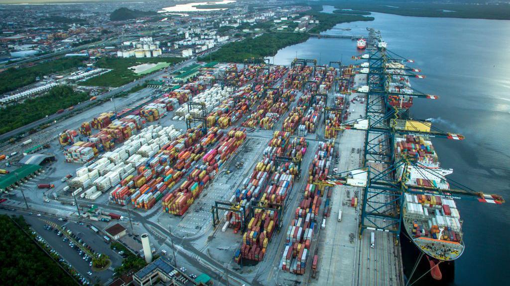 Porto de Santos visto do alto, com pilas de contêineres e navio sendo carregado 