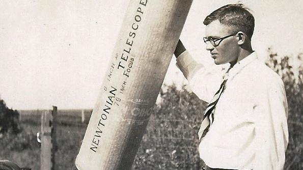 Foto em preto e branco mostra Clyde W. Tombaugh de perfil ao lado de telescópio