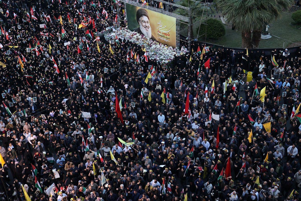 Imagem aérea de centenas de pessoas reunidas ao redor de uma foto grande do líder do Hezbollah, Sayyed Hassan. 