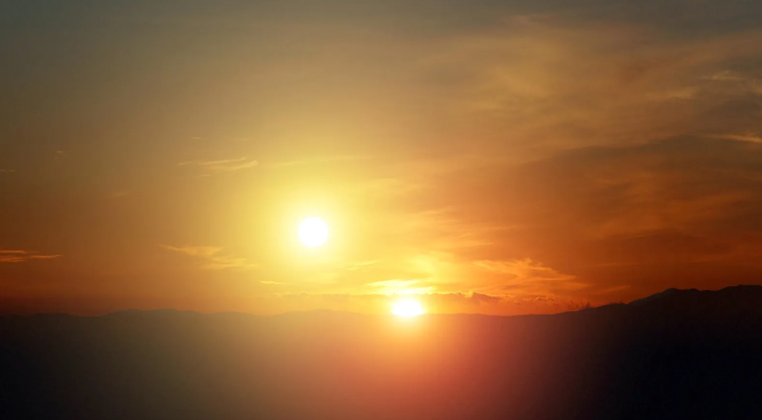 Dois sóis brilhando no céu durante o pôr do sol, com montanhas no horizonte e um céu laranja ao fundo.