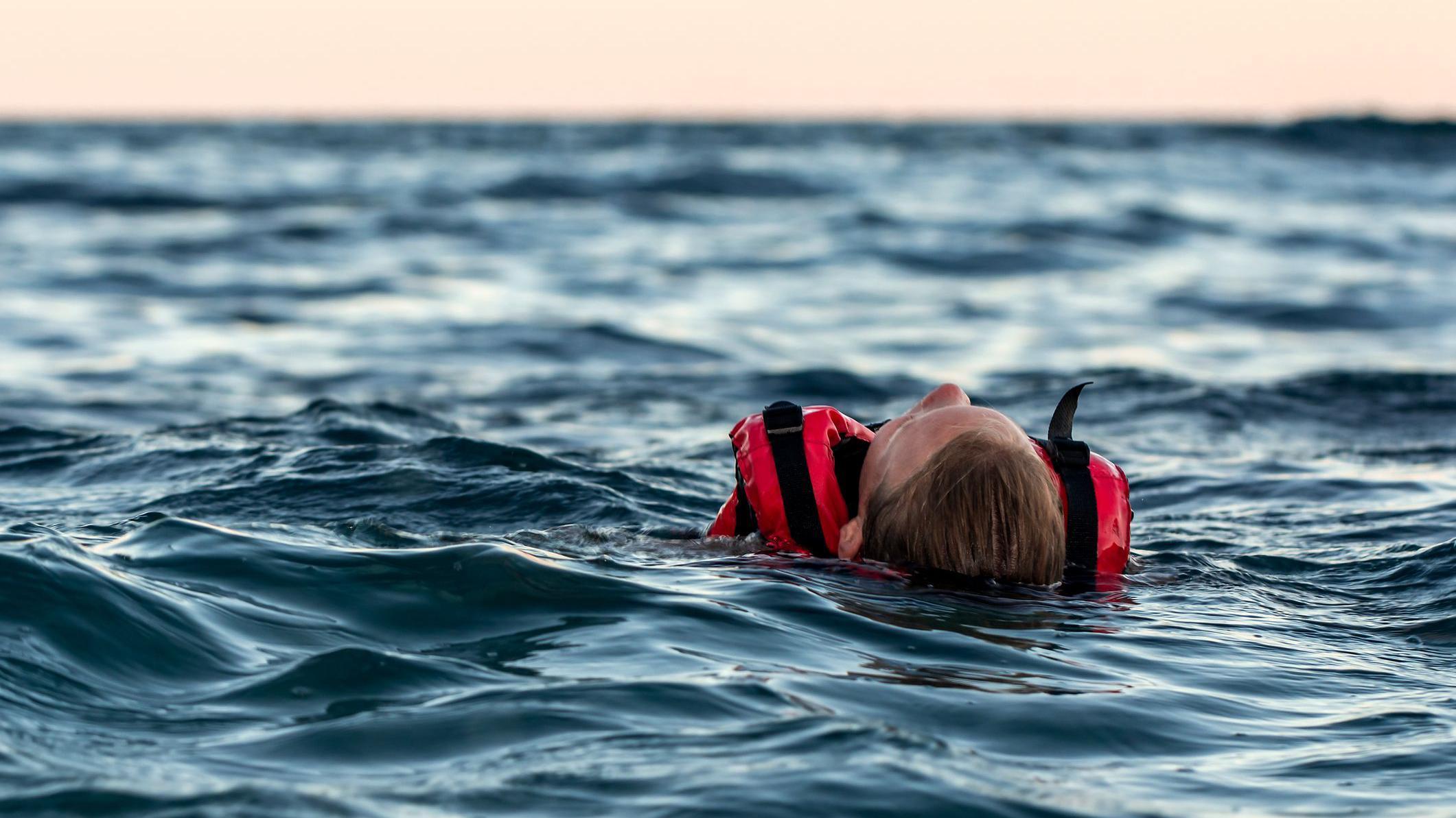 Una joven flotando con un chaleco salvavidas en el medio de un mar frío mientras se acerca el anochecer.