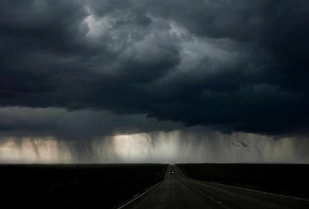 Carro passando em estrada em ambiente escuro e com nuvens pesadas atrás