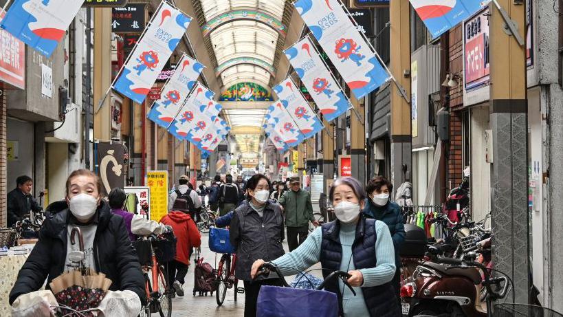 Mulheres com máscaras empurram suas bicicletas nas ruas do Japão