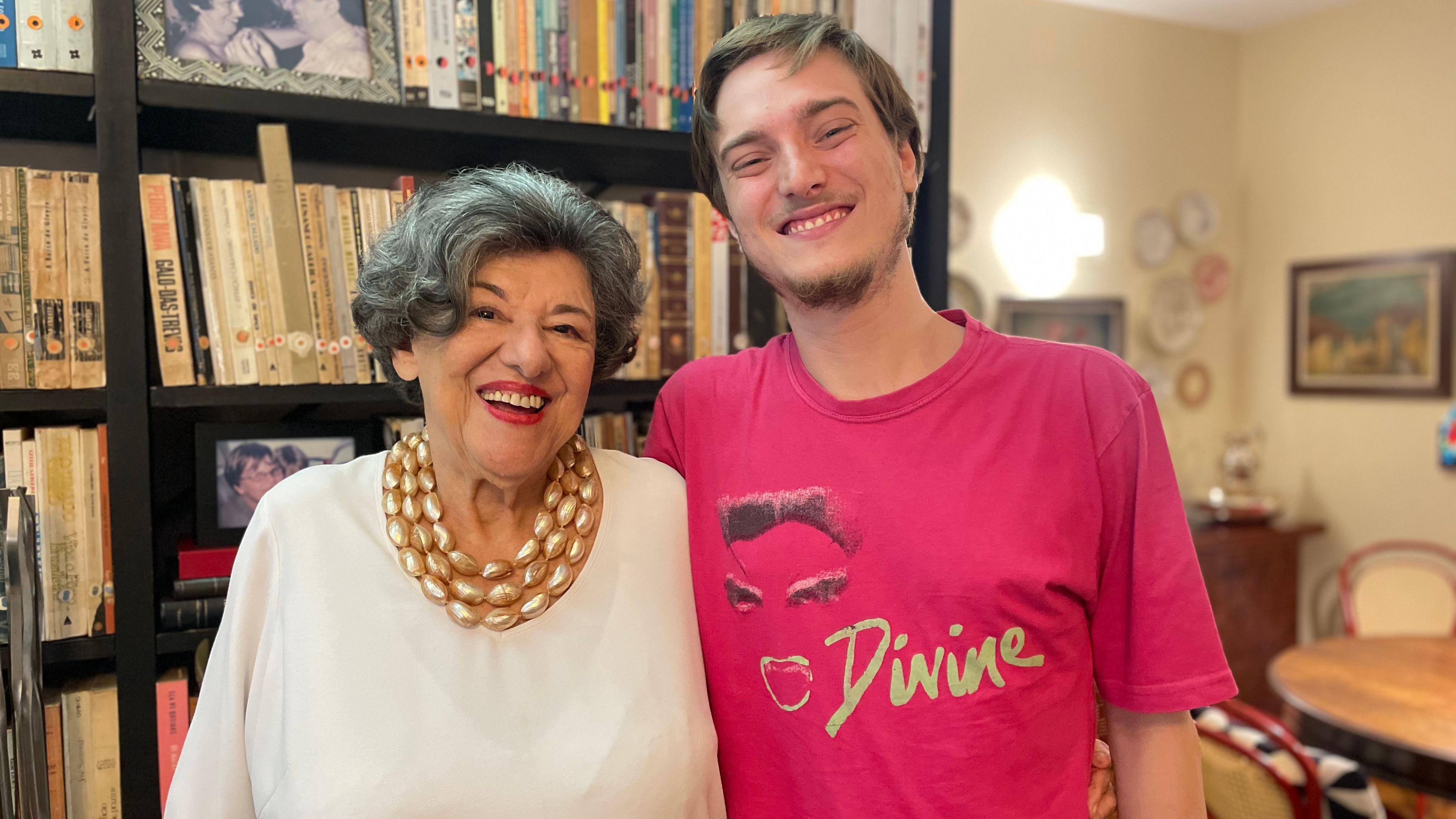 Ruth e Pedro sorrindo, abraçados, em frente a estante de livros