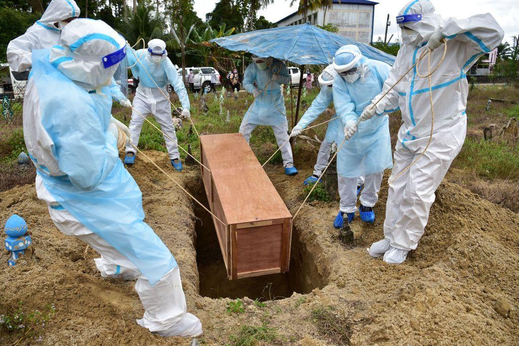 Trabajadores con equipos de protección individual (EPI) entierran en un cementerio a un voluntario civil de defensa fallecido a causa de Covid-19 en Tailandia..