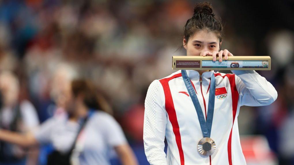 Atleta chinês com medalha de bronze e mão no rosto