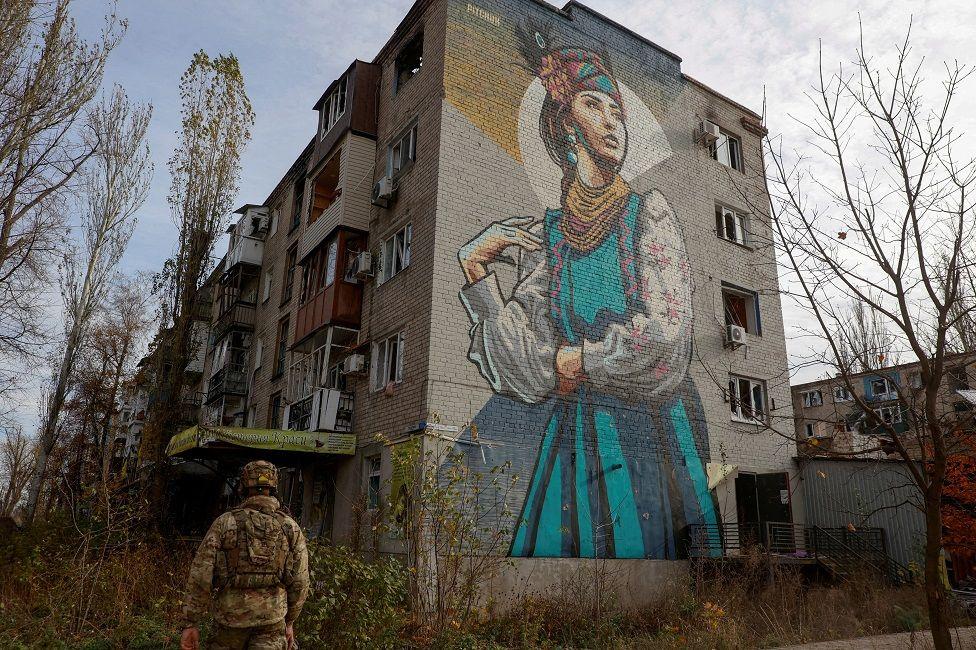 Un soldado ucranino pasaba por un edificio con un mural de una mujer