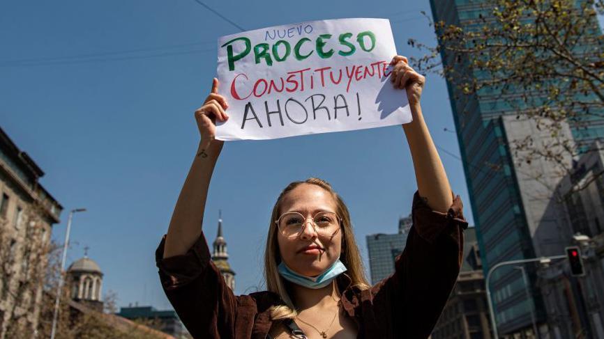Una mujer sostiene un cartel que pide cambio constitucional