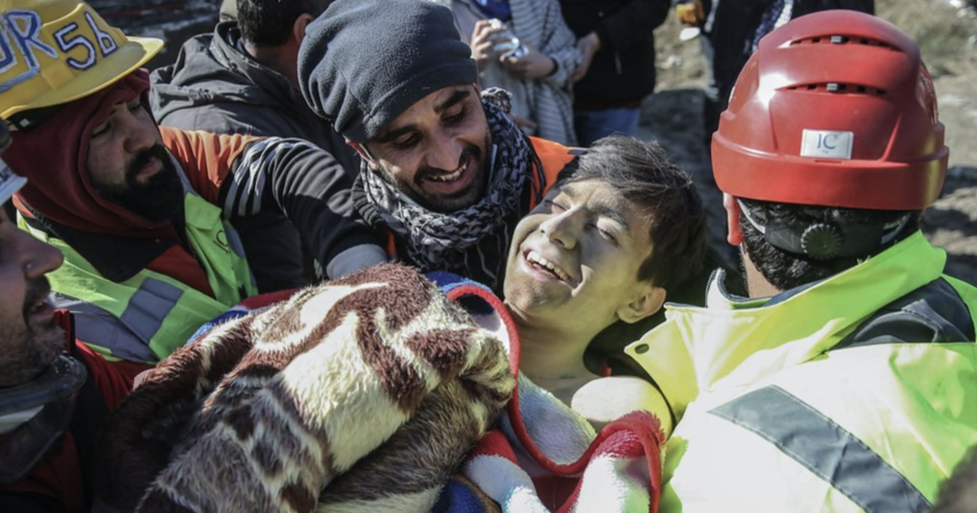 Um jovem rapaz sorri ao ser resgatado por socorristas
