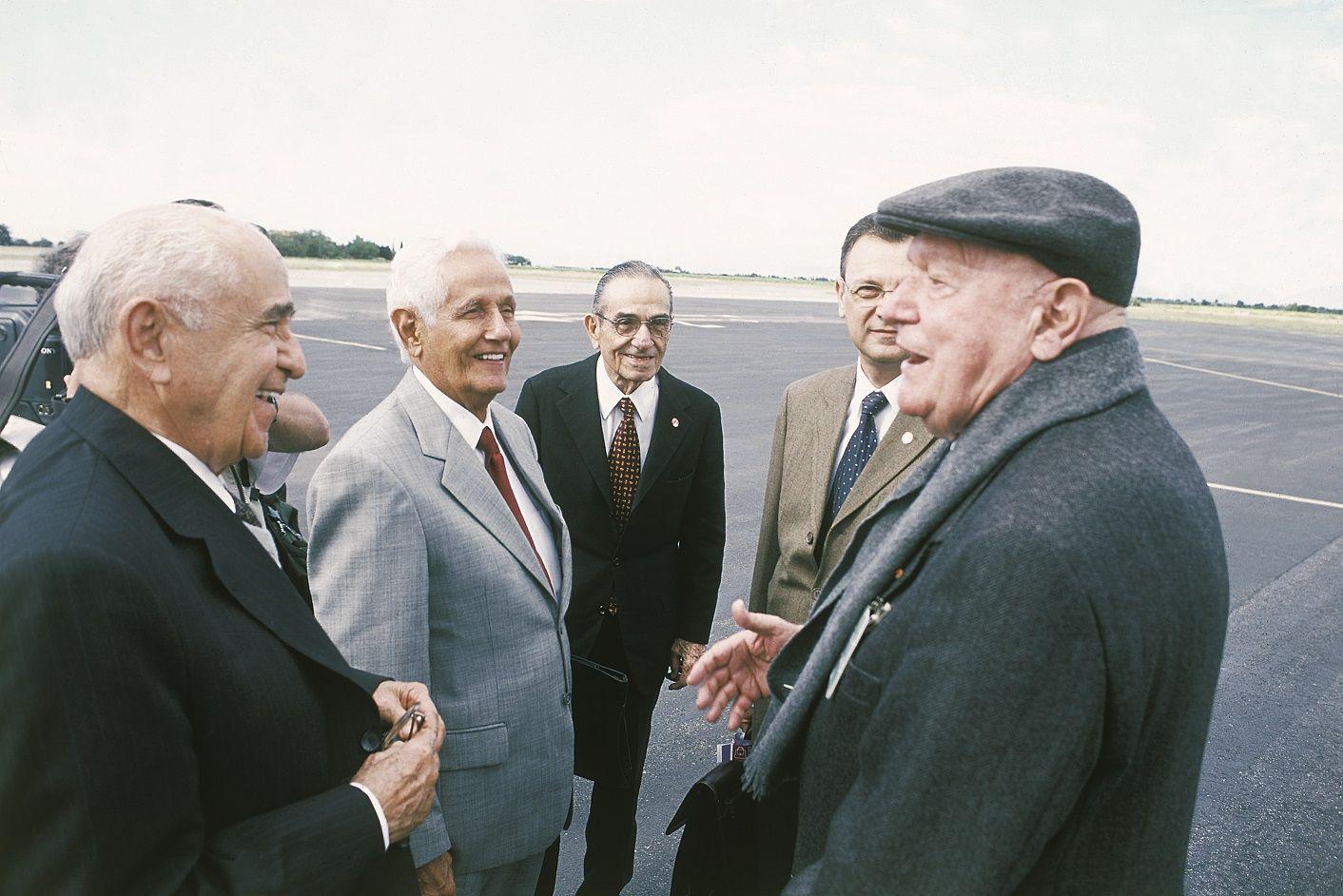 Cinco homens em roda conversando, em pista de aviões