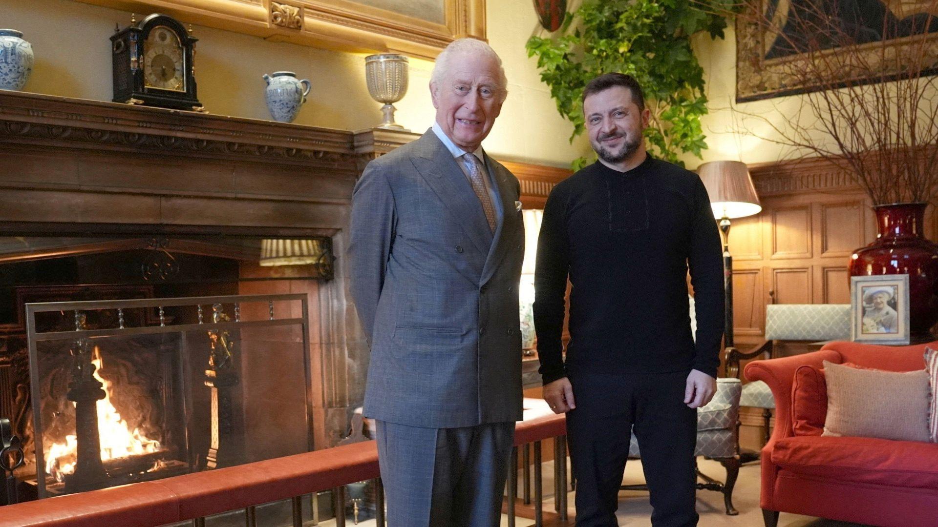 King Charles dressed in a grey suit stands in front of a chimney next to Ukrainian President Volodymr Zelensky who is dresses in all black fatigues.