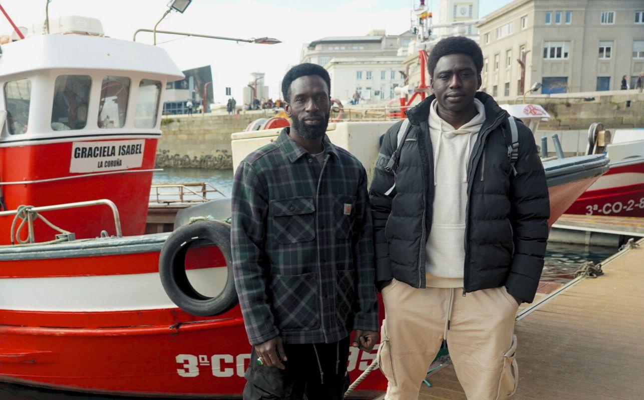 Ibrahima Diack y Magatte N´Diaye en el puerto deportivo de La Coruña con un barco rojo detrás. 