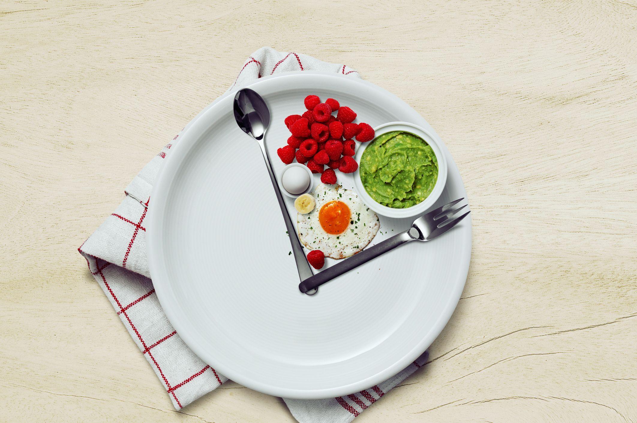 Plato de comida con un tenedor y una cuchara como agujas de un reloj y comida saludable en medio.