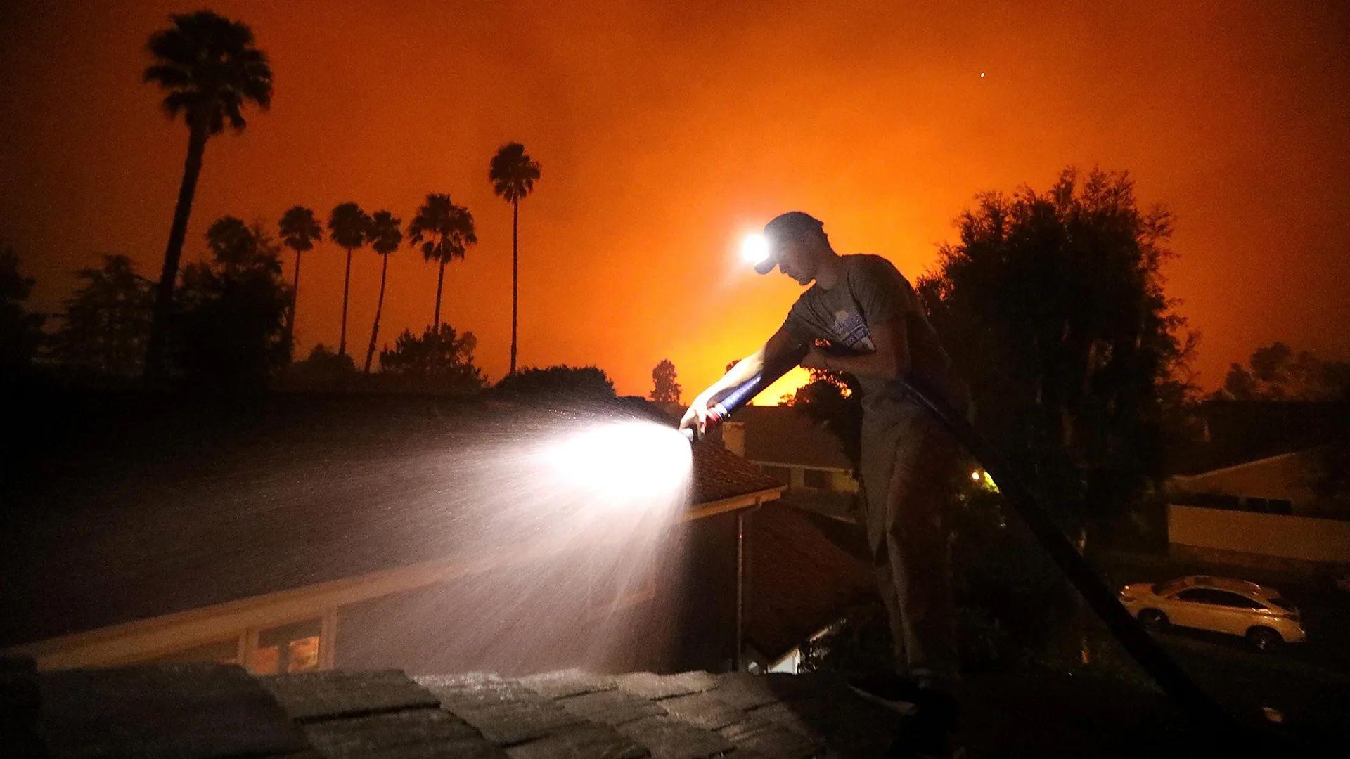 Una persona con una manguera intentando controlar los incendios en California