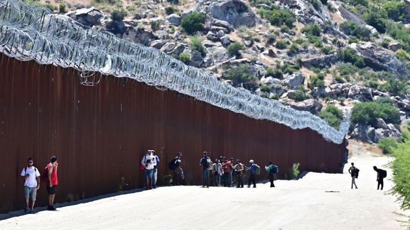 Migrantes entram nos EUA ao lado do muro da fronteira EUA-México em Jacumba Hot Springs, Califórnia, junho de 2024