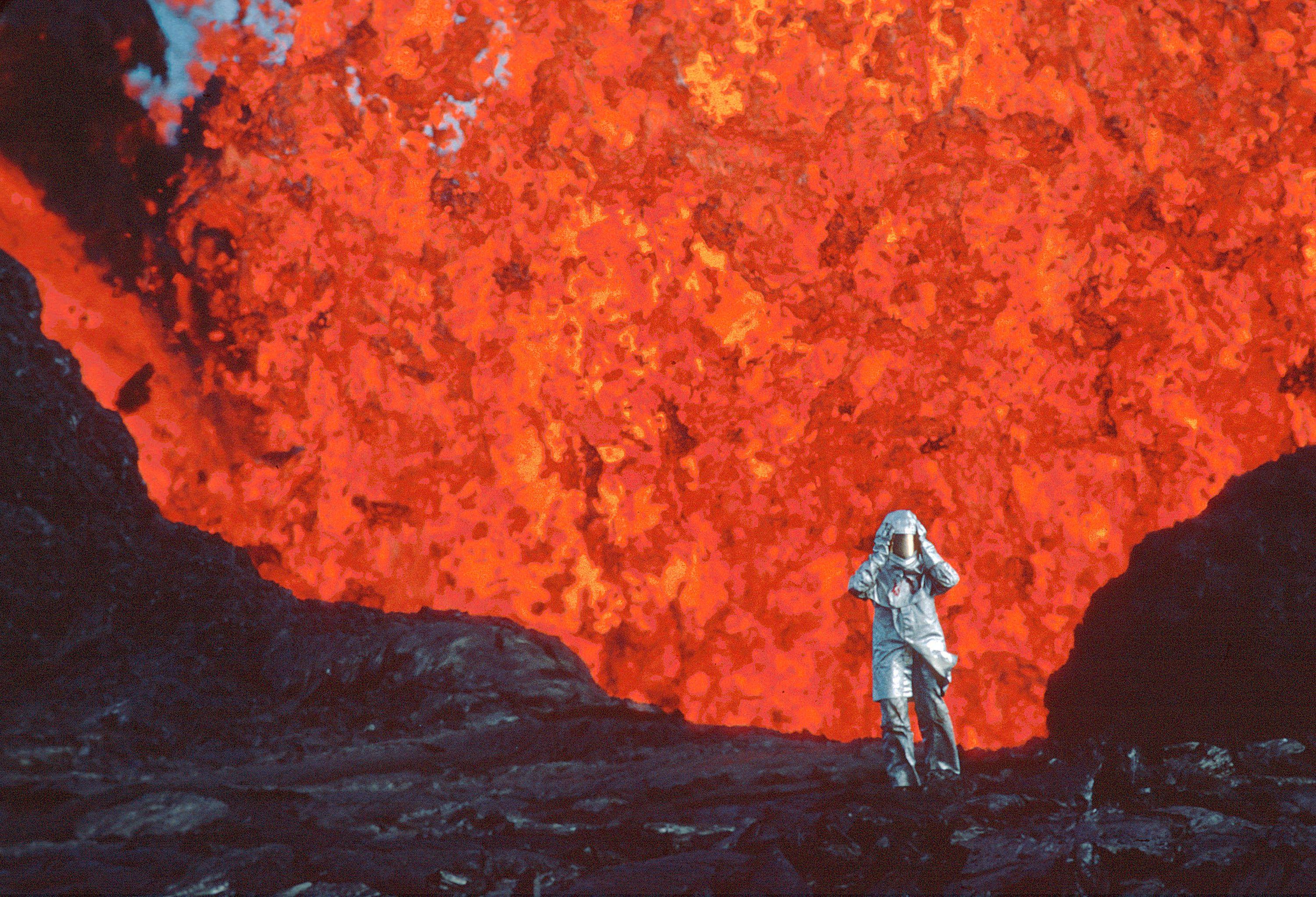 Katia Krafft aparece com roupa parecida com astronauta, na frente de lava vulcânica vermelha