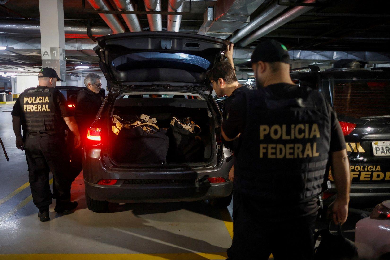 Policiais em volta de carro, que tem porta-malas cheio de malas com apreensões