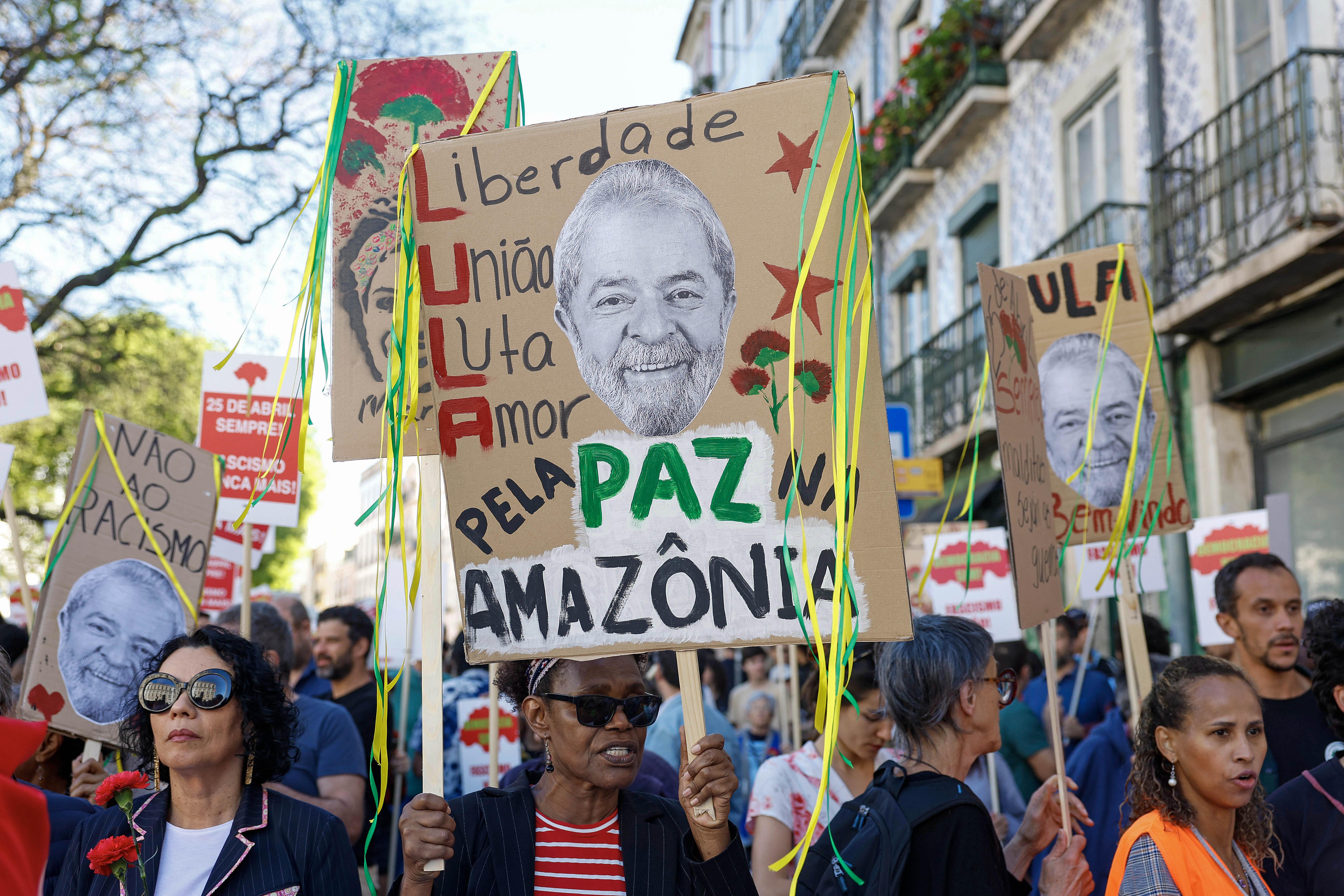 Na rua, mulher levanta cartaz com rosto de Lula e dizeres: 