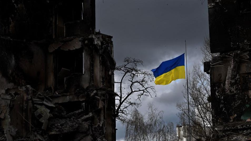 The Ukrainian flag flutters between buildings destroyed in bombardment, in the Ukrainian town of Borodianka, in the Kyiv region on April 17, 2022. - Russia invaded Ukraine on February 24, 2022