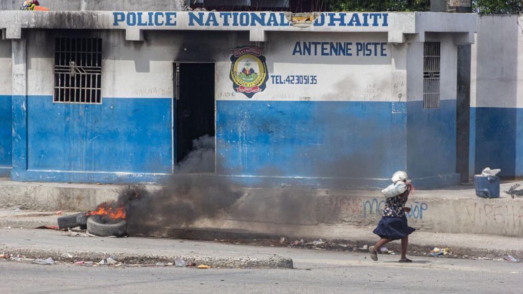 una mujer corre frente a un cuartel de la policía en Haití 