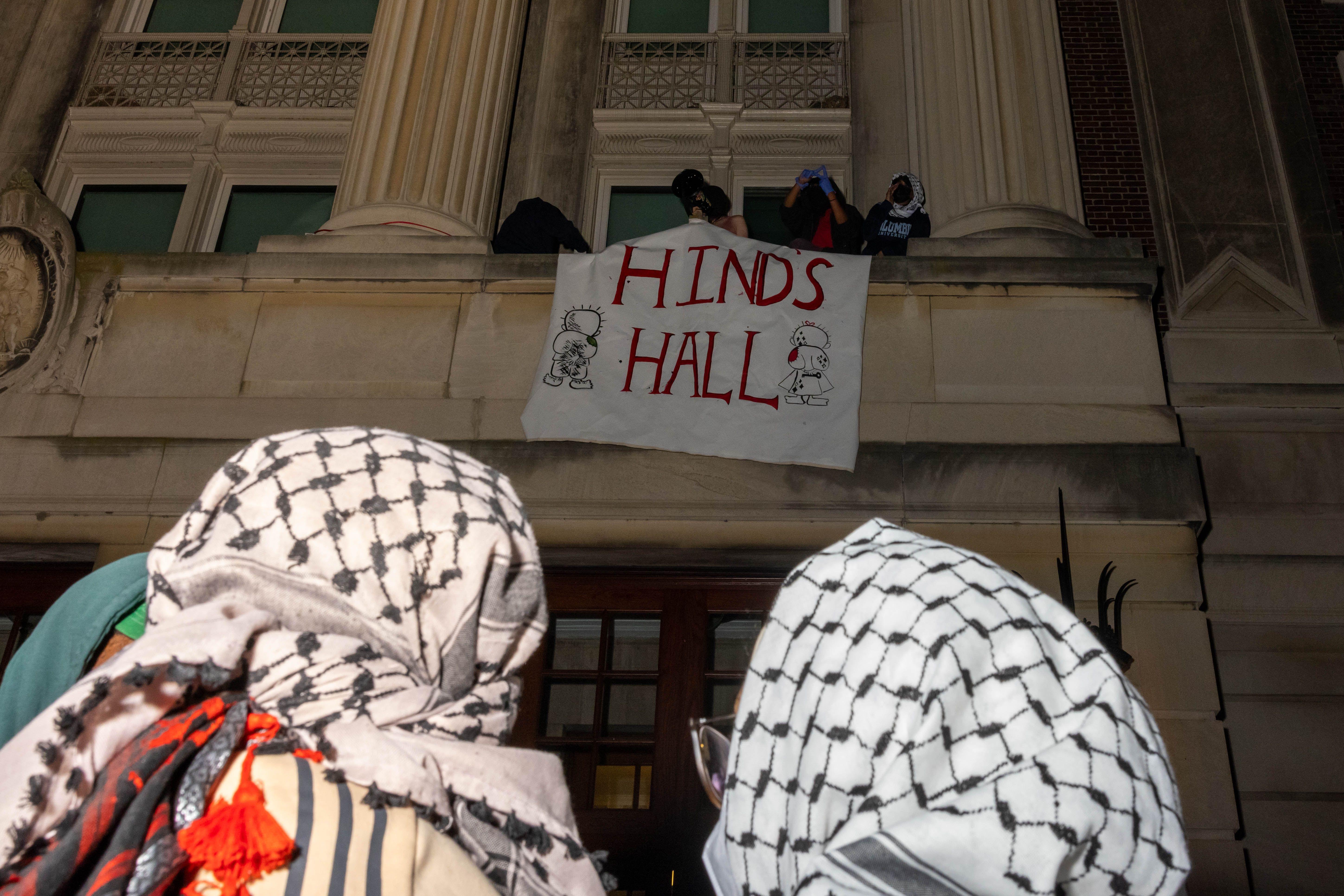 Manifestantes con pañuelos palestinos en la cabeza ven como ocupantes del edificio colocan un cartel en un balcón que dice "Hind's Hall", es decir, "Sala de Hind"