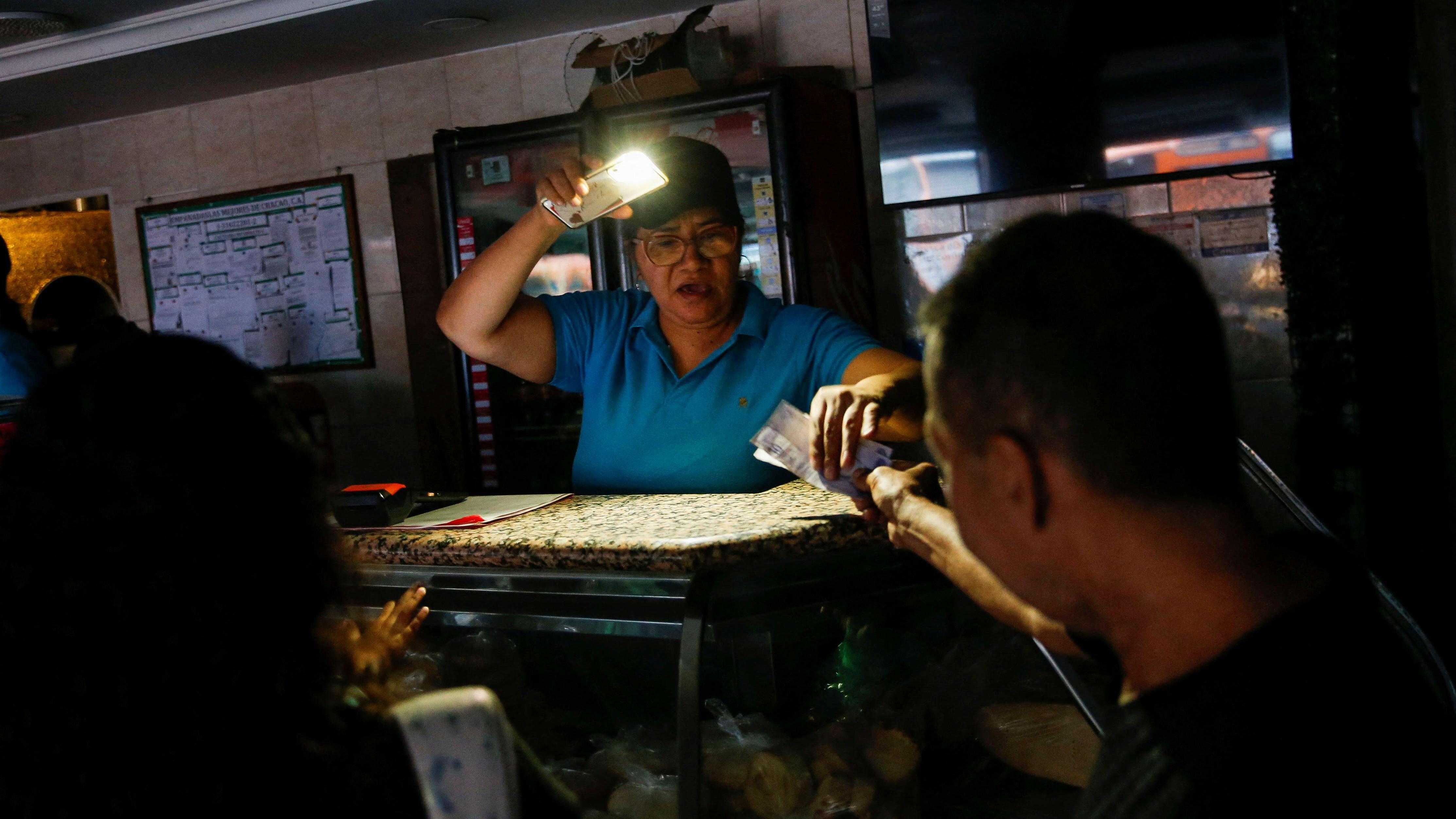 Un mujer vende comida e ilumina con su celular. 