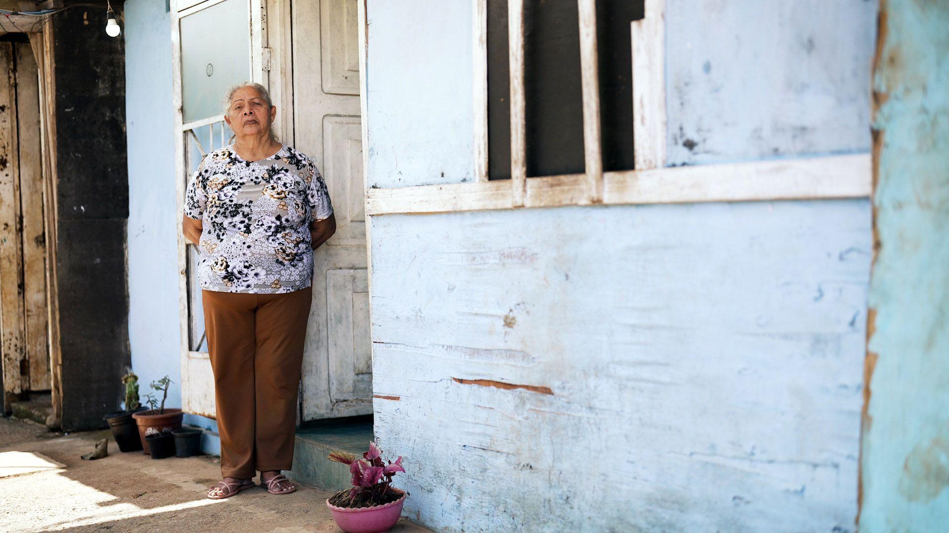 Carmen Noriega, uma mulher de 72 anos, em frente ao seu barraco de madeira pintada de azul