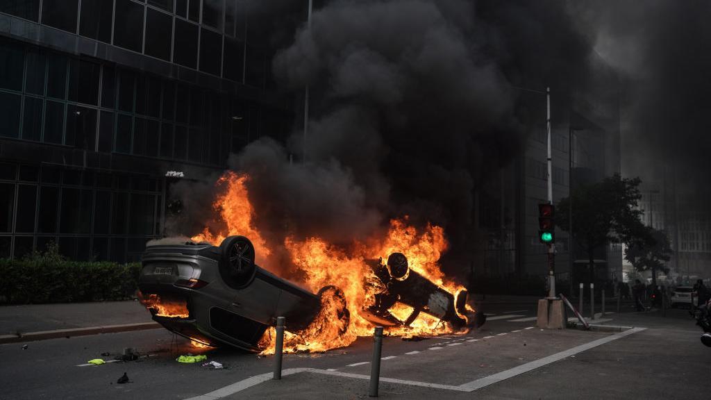 Un automóvil volcado se quema durante los enfrentamientos entre las fuerzas policiales francesas y los jóvenes después de una marcha en memoria del adolescente francés Nahel