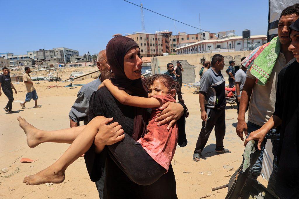 امرأة فلسطينية تحمل طفلاً مصاباً إلى مستشفى ناصر، في خان يونس في 13 يوليو/تموز 2024،  جراء غارة إسرائيلية قتلت ما لا يقل عن 90 شخصاً وأصابت قرابة 300 شخص في مخيم المواصي للاجئين.