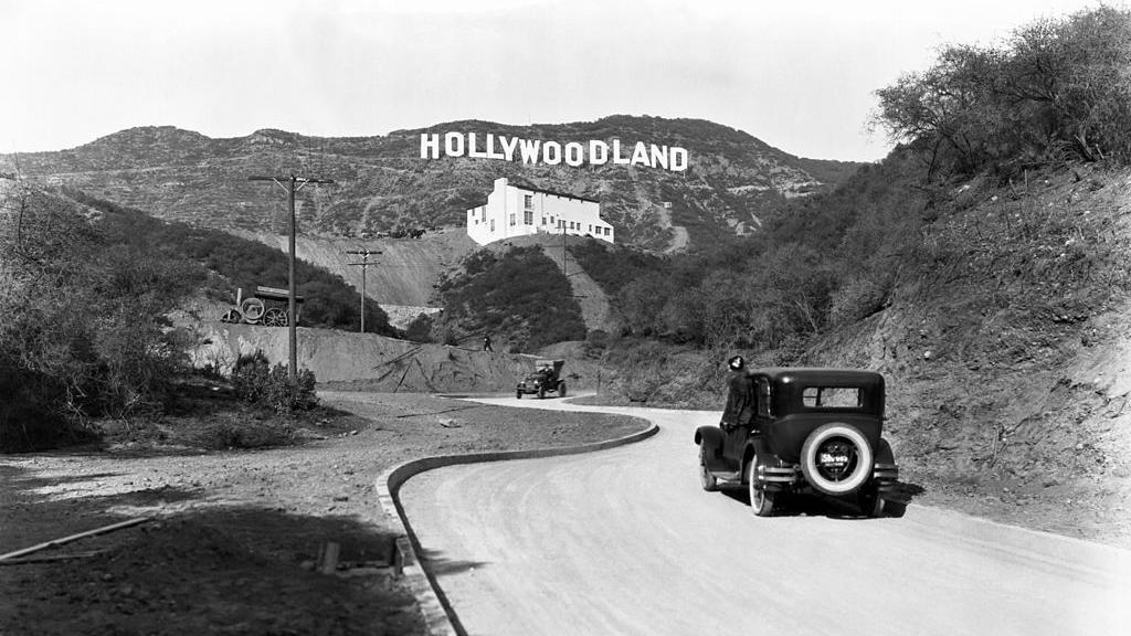 Un cartel anuncia la apertura del desarrollo de viviendas Hollywoodland en las colinas de Mulholland Drive con vistas a Los Ángeles, Hollywood, Los Ángeles, California, alrededor de 1924. El edificio blanco debajo del cartel es la Galería de Arte Kanst, que abrió sus puertas el 1 de abril de 1924.