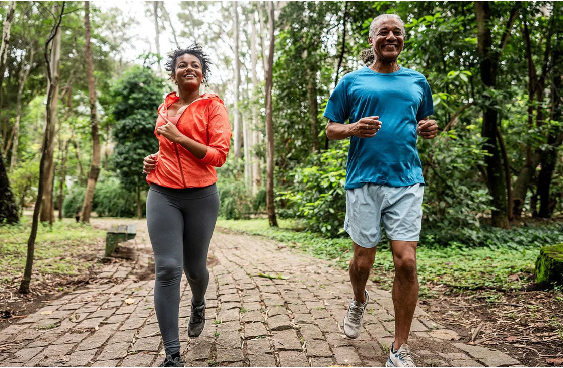 Duas pessoas correm em uma pista de caminhada, com paisagem verde ao fundo