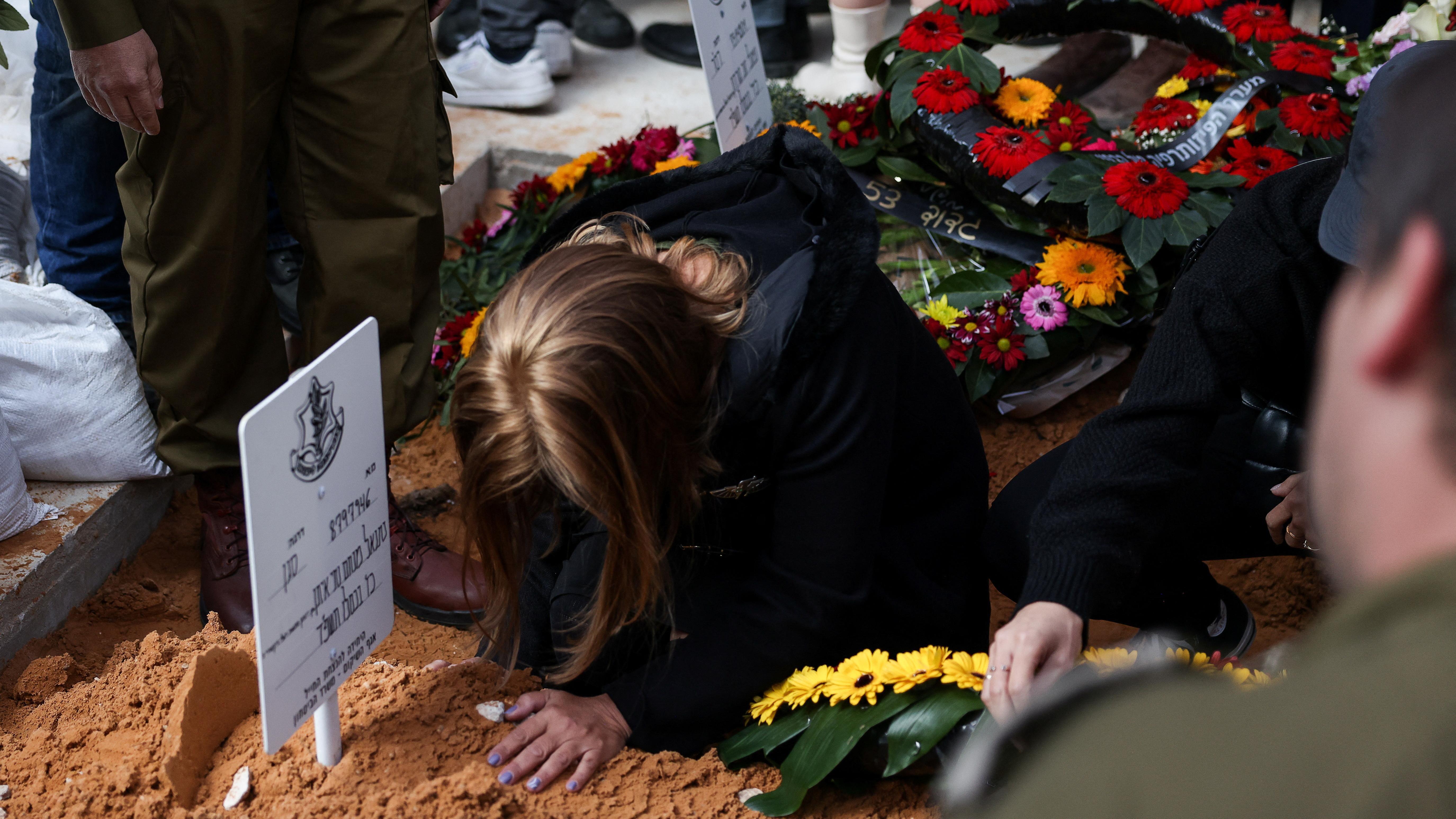 Uma mulher, com a cabeça inclinada, toca a terra de um túmulo no funeral de um soldado de reserva israelense, em Jerusalém