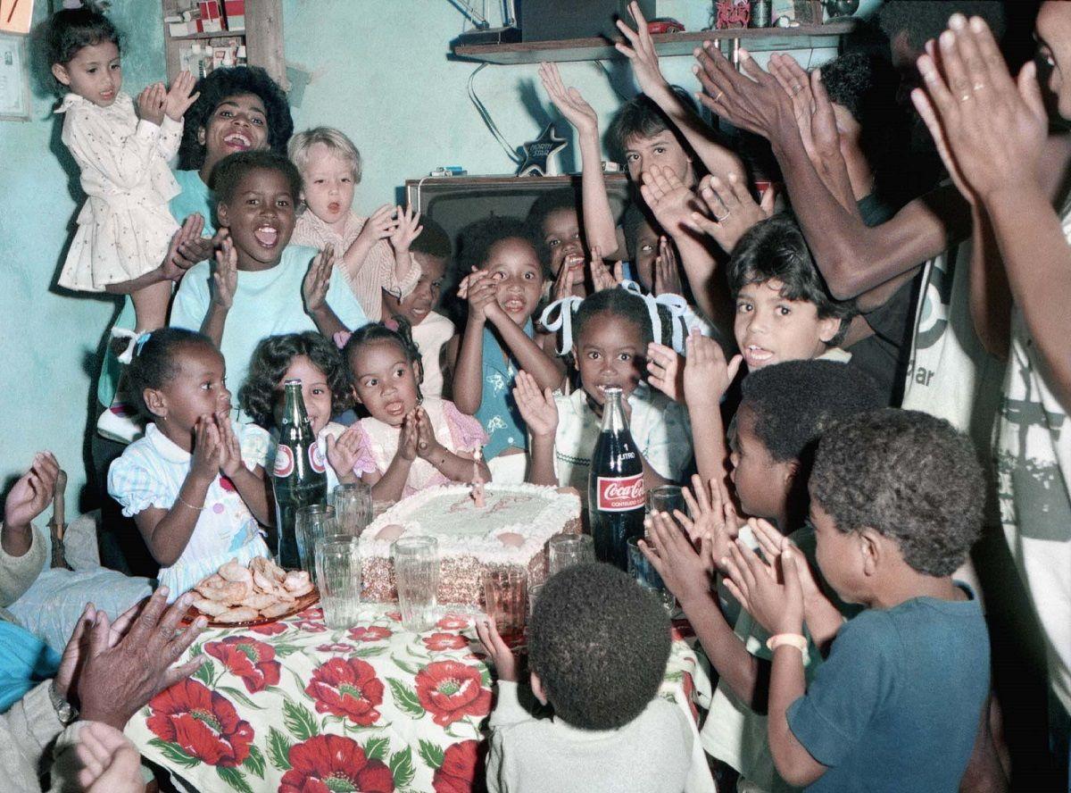 Crianças e adultos cantando parabéns em volta do bolo