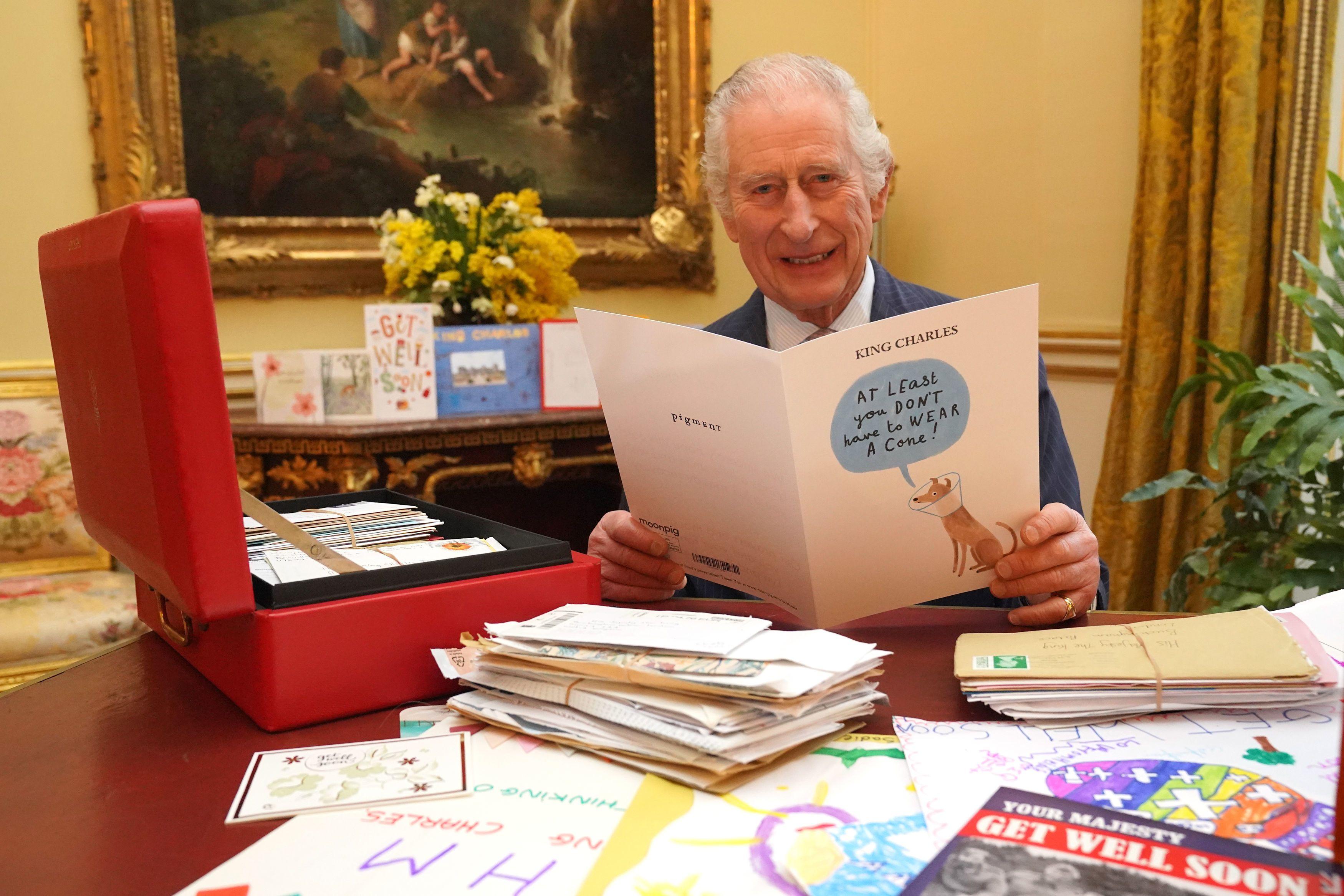 King Charles posing at his desk with a series of get well soon cards