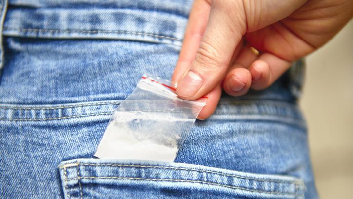 Mão feminina colocando saquinho de plástico com substância branca no bolso na calça jeans