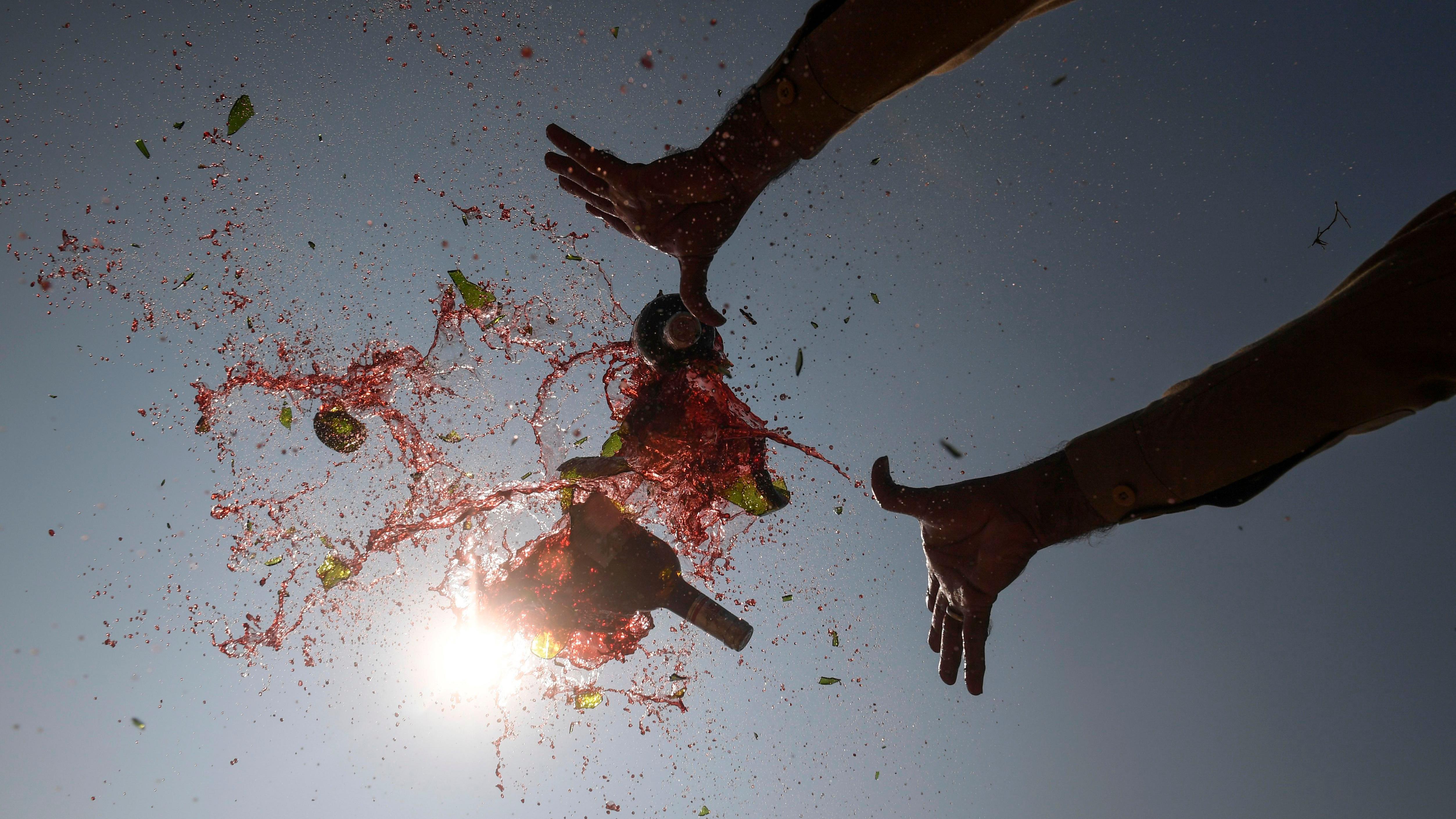 Alcoholic beverages spray into the air as an official smashes seized bottles, previously smuggled into the country, on the outskirts of Karachi on 3 December 2019