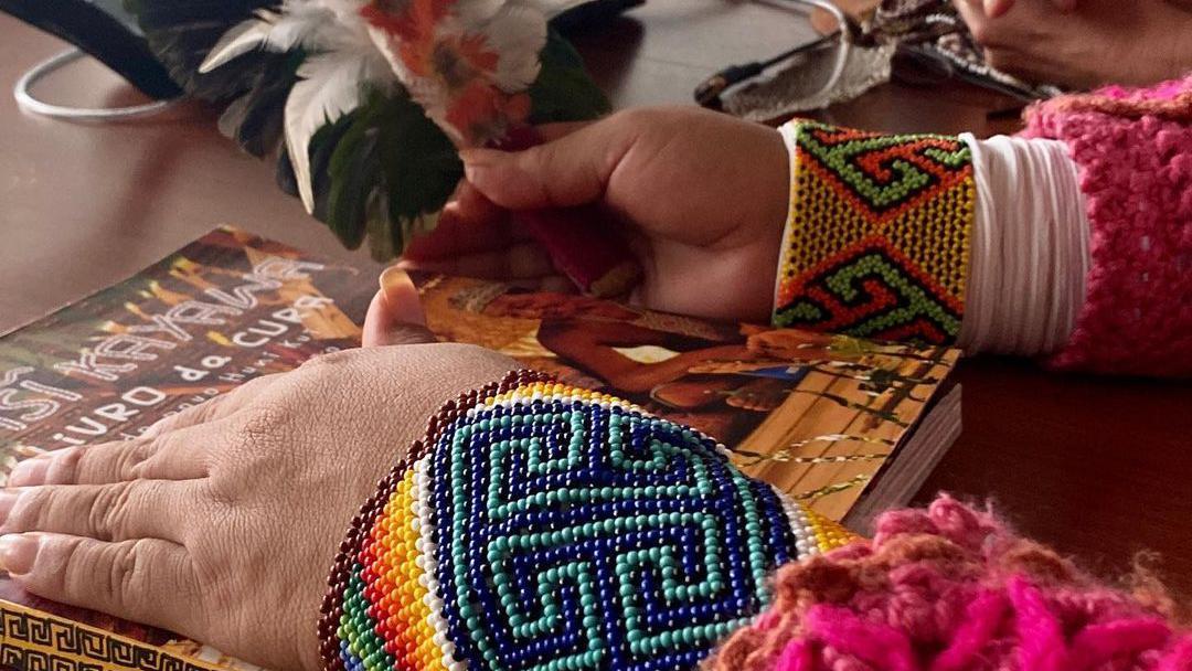 Mão manuseando livro, com decorações indígenas