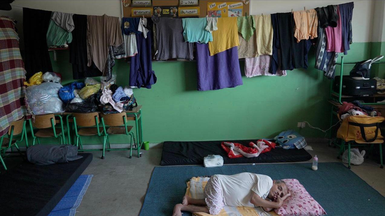 Uma senhora idosa está deitada em um colchão com roupas penduradas ao redor dela