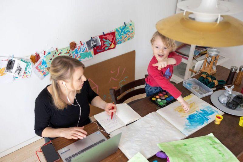 بچہ کتاب میں رنگ کر رہا ہے جبکہ اس کے ساتھ بیٹی عورت اپنے کام کے دوران اس کو توجہ دیتی ہیں