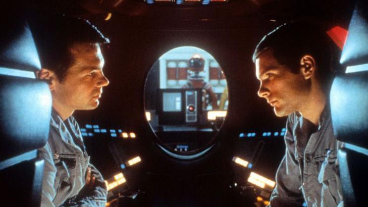 Los astronautas Poole y Bowman dentro de una cápsula con la lente roja de HAL en el fondo