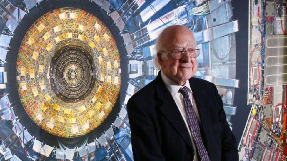 Na foto, Peter Higgs é um senhor de pele clara, pouco cabelo, usando óculos, terno escuro sobre camisa branca e gravata. 